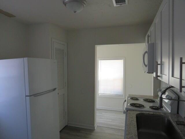 kitchen featuring visible vents, freestanding refrigerator, a sink, wood finished floors, and baseboards