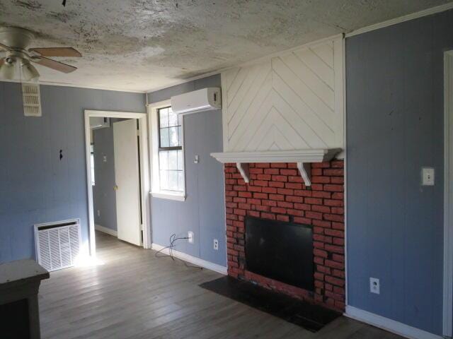 unfurnished living room with a wall mounted AC, a brick fireplace, wood finished floors, and visible vents