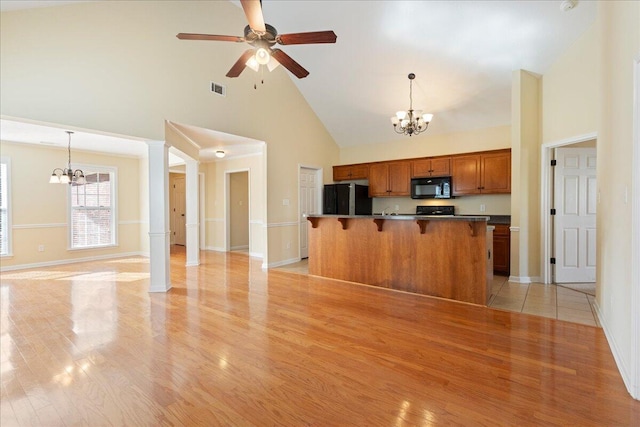 kitchen with black appliances, decorative light fixtures, a kitchen bar, and high vaulted ceiling