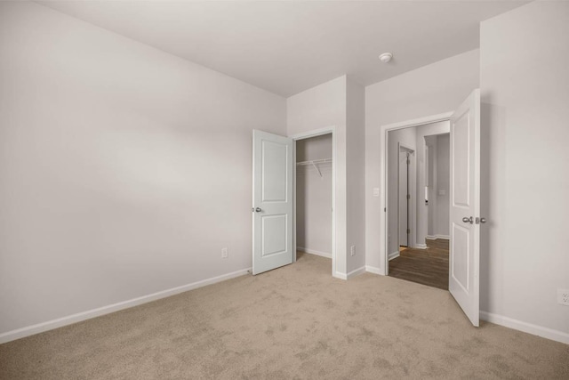 unfurnished bedroom with a closet, light colored carpet, and baseboards