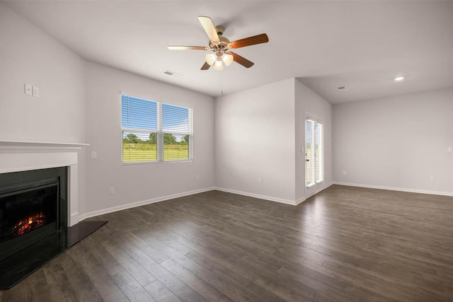 unfurnished living room featuring a wealth of natural light, visible vents, dark wood-type flooring, and a glass covered fireplace