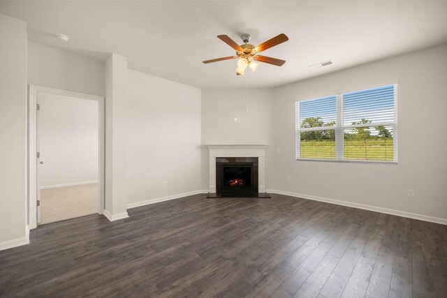 unfurnished living room featuring visible vents, ceiling fan, baseboards, a lit fireplace, and dark wood-style flooring