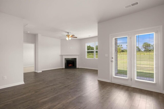 unfurnished living room featuring a ceiling fan, dark wood-style floors, visible vents, baseboards, and a fireplace with flush hearth