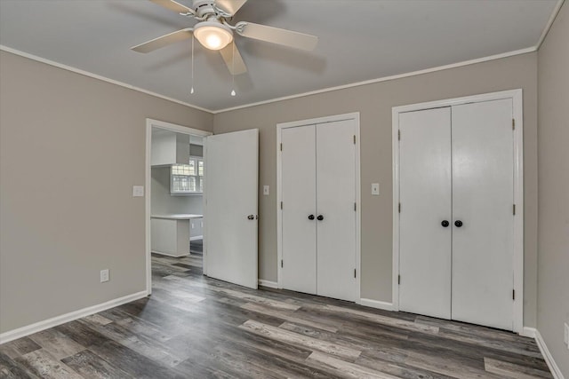 unfurnished bedroom with ceiling fan, dark hardwood / wood-style floors, crown molding, and multiple closets