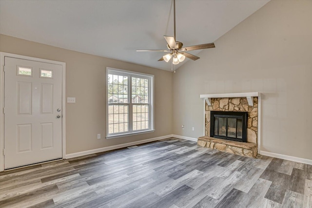 unfurnished living room with ceiling fan, a stone fireplace, light wood-type flooring, and vaulted ceiling