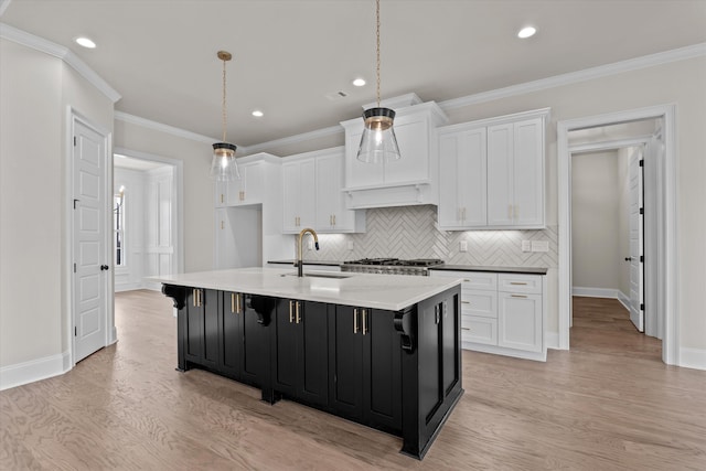 kitchen with a sink, white cabinetry, light wood-style floors, an island with sink, and recessed lighting