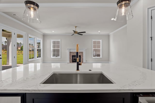 kitchen with open floor plan, a sink, light stone counters, ceiling fan, and healthy amount of natural light