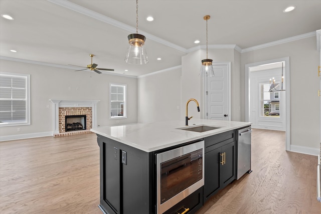 kitchen with a sink, appliances with stainless steel finishes, light wood finished floors, dark cabinetry, and recessed lighting