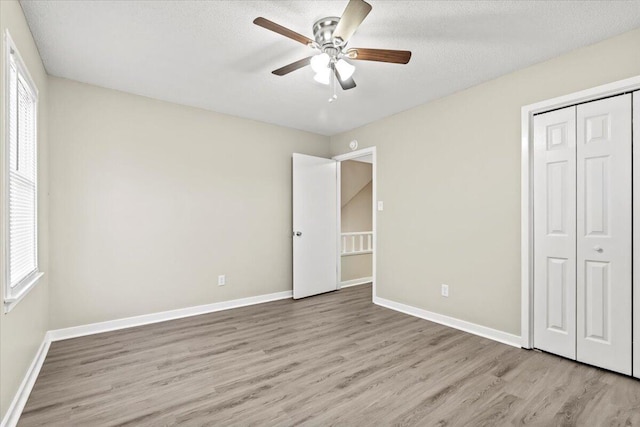 unfurnished bedroom with a textured ceiling, light hardwood / wood-style flooring, a closet, and ceiling fan