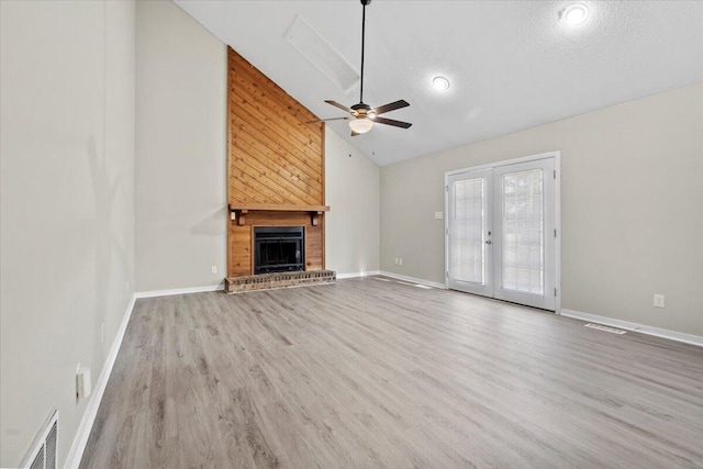 unfurnished living room featuring high vaulted ceiling, a fireplace, a textured ceiling, french doors, and light wood-type flooring