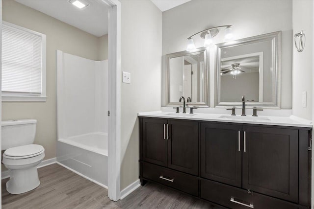 full bathroom featuring wood-type flooring, vanity, ceiling fan, toilet, and washtub / shower combination