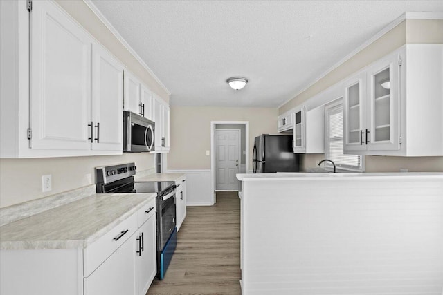 kitchen featuring wood-type flooring, a textured ceiling, ornamental molding, appliances with stainless steel finishes, and white cabinets