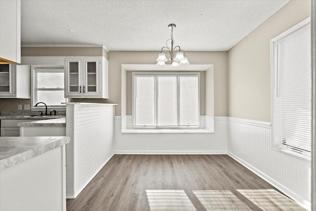 unfurnished dining area with sink, a notable chandelier, a textured ceiling, and light hardwood / wood-style flooring