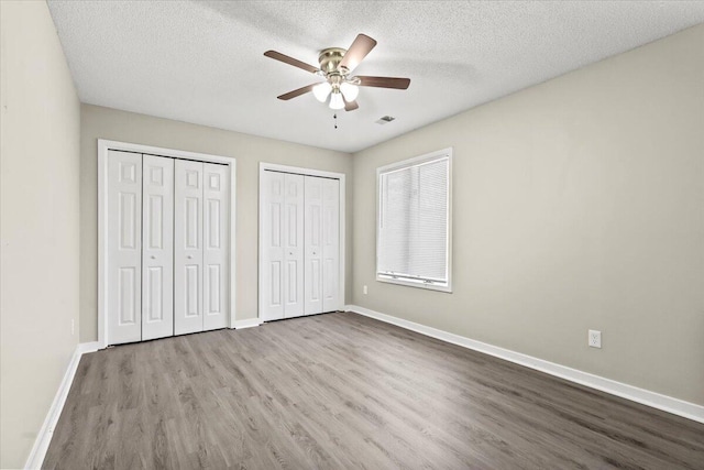 unfurnished bedroom featuring multiple closets, light wood-type flooring, a textured ceiling, and ceiling fan