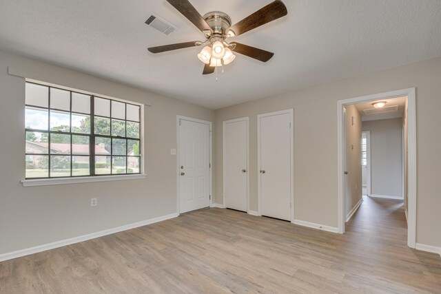 spare room featuring ceiling fan with notable chandelier, light hardwood / wood-style floors, and a textured ceiling