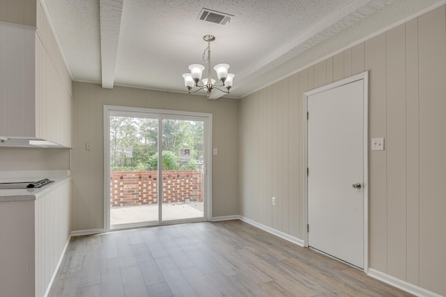 unfurnished dining area with a textured ceiling, wood walls, light hardwood / wood-style flooring, and an inviting chandelier