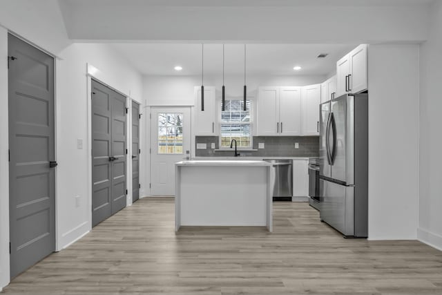 kitchen featuring stainless steel appliances, light countertops, hanging light fixtures, white cabinetry, and a kitchen island