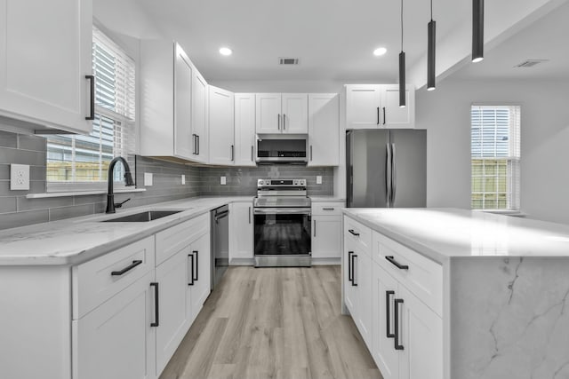 kitchen featuring appliances with stainless steel finishes, white cabinets, a sink, and hanging light fixtures