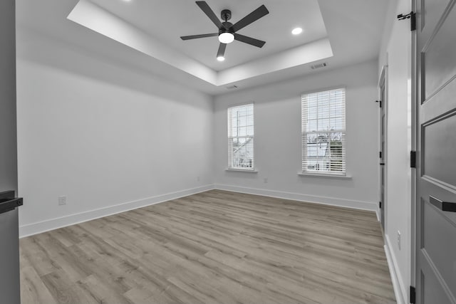 spare room featuring light wood finished floors, baseboards, visible vents, a raised ceiling, and ceiling fan