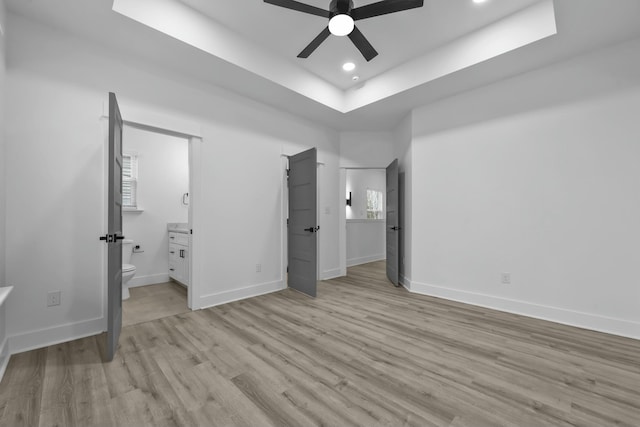 unfurnished bedroom featuring a tray ceiling, light wood-style flooring, baseboards, and recessed lighting