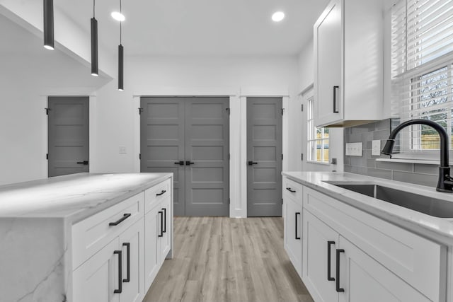 kitchen featuring pendant lighting, light stone counters, a sink, and white cabinets