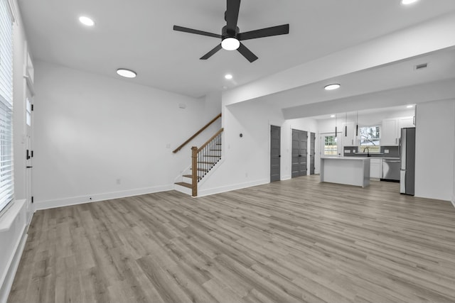 unfurnished living room featuring light wood-type flooring, visible vents, stairway, and ceiling fan