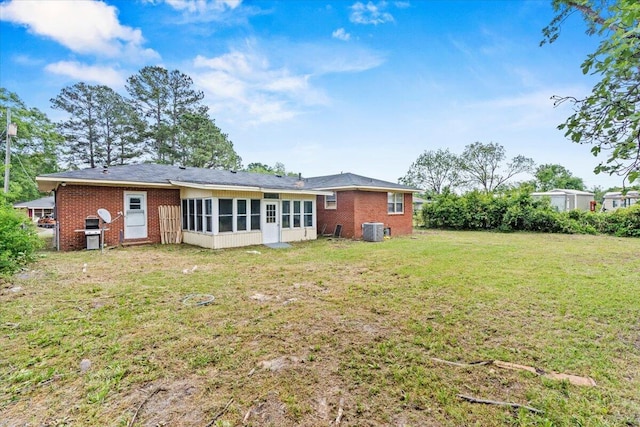 rear view of house with a lawn, a sunroom, cooling unit, and brick siding