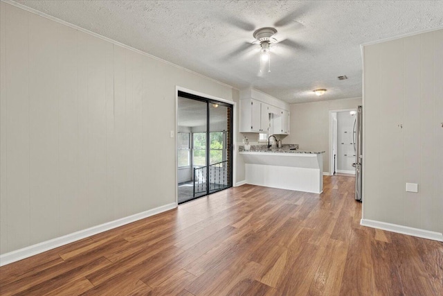 unfurnished living room with a ceiling fan, a textured ceiling, crown molding, wood finished floors, and a sink