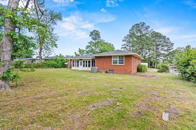 back of property featuring brick siding, a lawn, central AC, and fence