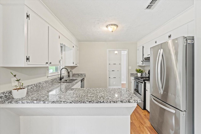 kitchen featuring a textured ceiling, a sink, a peninsula, light wood-style floors, and stainless steel appliances