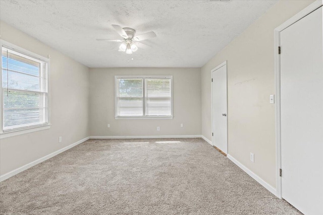 empty room featuring a textured ceiling, ceiling fan, light colored carpet, and baseboards