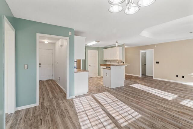 kitchen with open floor plan, white cabinets, light wood-type flooring, and baseboards