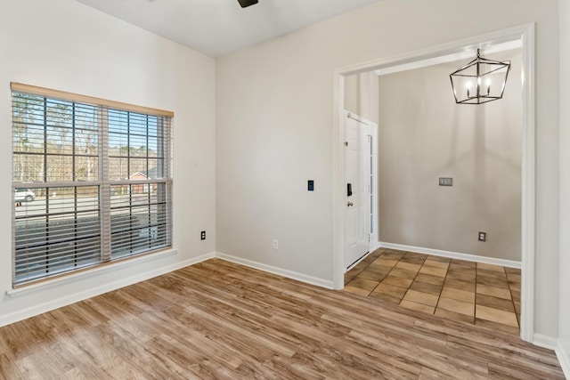 spare room with baseboards, light wood-style floors, and ceiling fan with notable chandelier