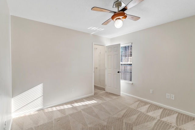 spare room featuring a ceiling fan, light colored carpet, and baseboards