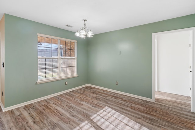 spare room with visible vents, baseboards, an inviting chandelier, and wood finished floors