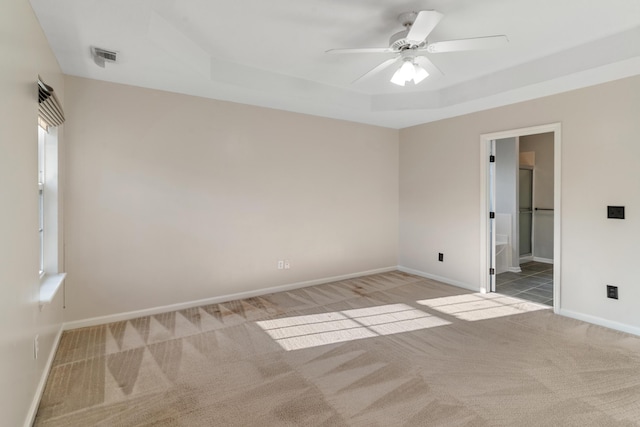 unfurnished room featuring visible vents, a ceiling fan, a tray ceiling, carpet flooring, and baseboards