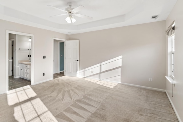 unfurnished bedroom featuring visible vents, a ceiling fan, baseboards, carpet flooring, and a raised ceiling