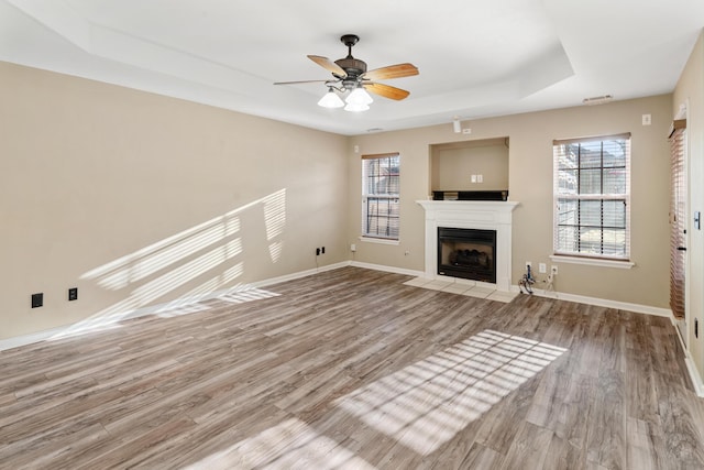 unfurnished living room featuring a fireplace with flush hearth, a healthy amount of sunlight, baseboards, and wood finished floors