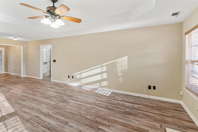 unfurnished room featuring a ceiling fan, a tray ceiling, wood finished floors, and baseboards