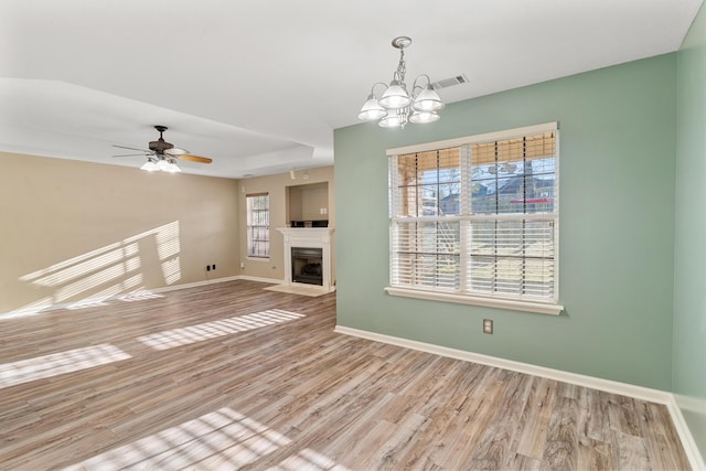 unfurnished living room featuring wood finished floors, visible vents, baseboards, a fireplace with flush hearth, and ceiling fan with notable chandelier