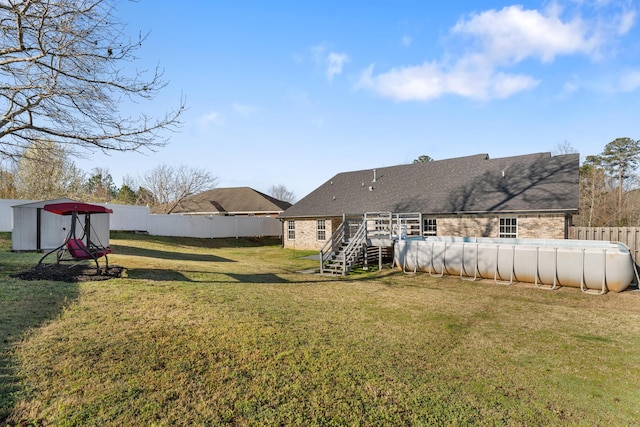 rear view of house with a fenced in pool, a fenced backyard, stairs, a lawn, and brick siding