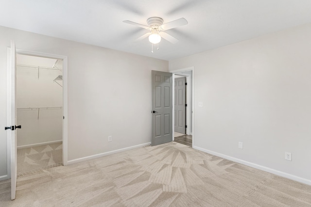 unfurnished bedroom with baseboards, ceiling fan, a closet, a walk in closet, and light colored carpet