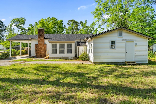 view of front of house featuring roof with shingles, a chimney, driveway, an attached carport, and a front yard