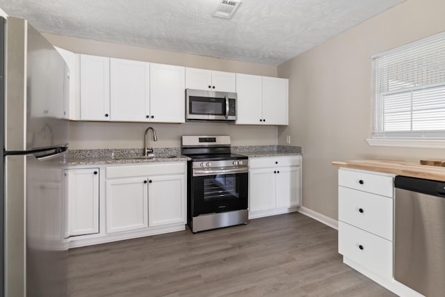 kitchen with light wood-style flooring, white cabinetry, visible vents, a sink, and stainless steel appliances