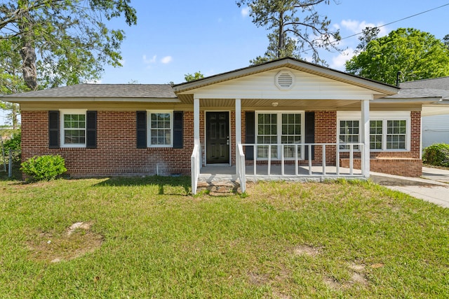 single story home with a shingled roof, covered porch, a front yard, and brick siding