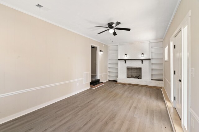 unfurnished living room with visible vents, built in features, a brick fireplace, ceiling fan, and wood finished floors