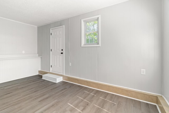 unfurnished room with a textured ceiling, wood finished floors, and ornamental molding