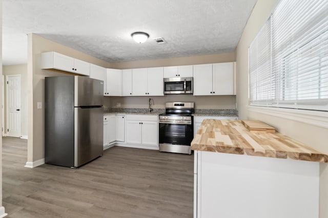 kitchen featuring a textured ceiling, white cabinetry, appliances with stainless steel finishes, wood finished floors, and wood counters