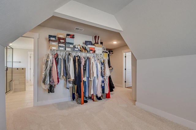 walk in closet with light colored carpet and vaulted ceiling