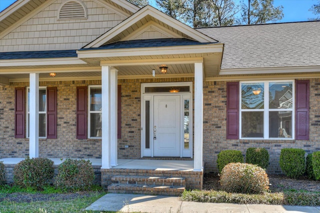 entrance to property with brick siding, roof with shingles, and a porch